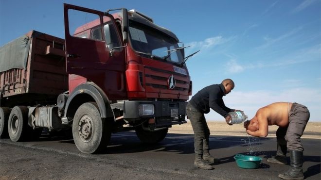Dos hombres se bañan con bidones de agua en la ruta.
