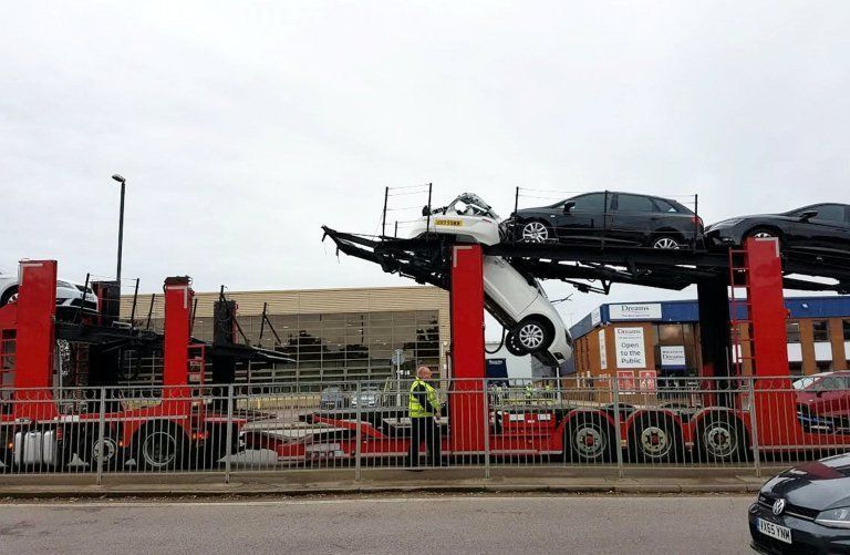 This is the scene of devastation after a vehicle transporter smashed into a bridge while stacked with pristine cars - tearing one in HALF. See SWNS story SWCAR. Dramatic photos show the front of a crushed white Seat hanging through the middle layer of the lorry while the rear end is left behind. The new car, thought to have a 2015 plate, was destroyed when the driver of the transporter misjudged the height of a new pedestrian footbridge. Office workers said they heard an "almighty crash" when cars on the top level collided with the bridge. Support engineer Richard Pithouse jumped up from his desk when he heard the commotion, on Gatwick Road, Crawley, at 10.30am on Friday.