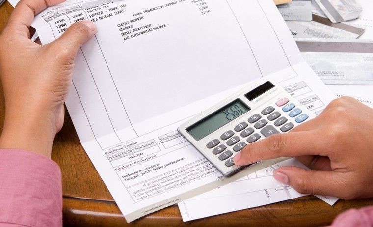 a woman calculation all the bills she have using a calculator. The number and personal ID of the credit card has been removed or replaced from the original one to prevent unnecessary things.