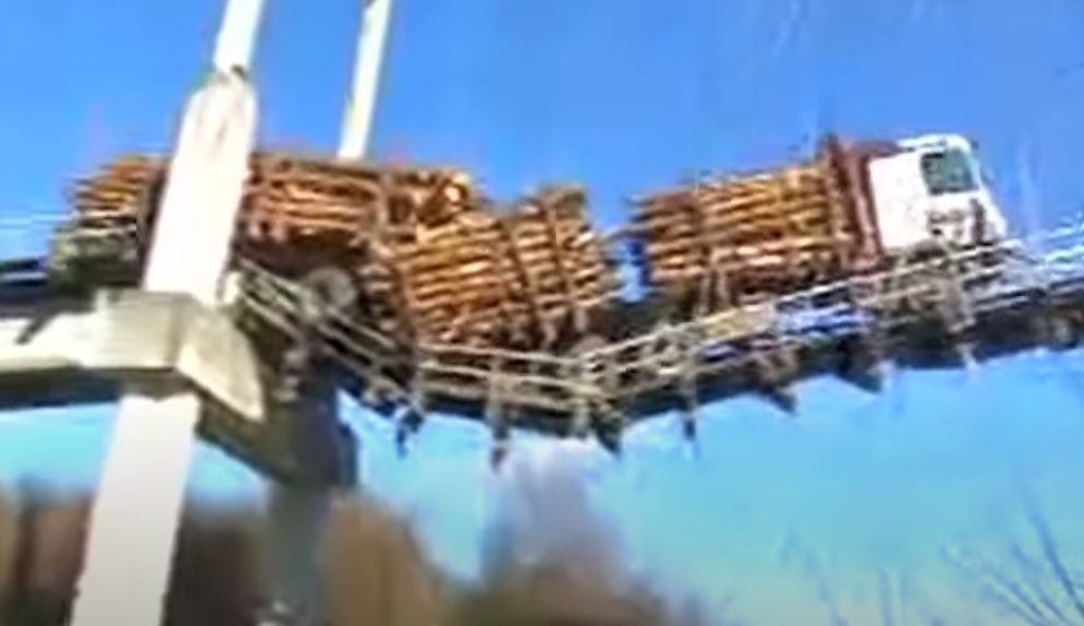 Un camión cargado de madera se queda colgando de un puente