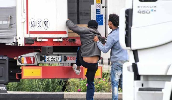 Imagen de dos inmigrantes intentando meterse en un camión